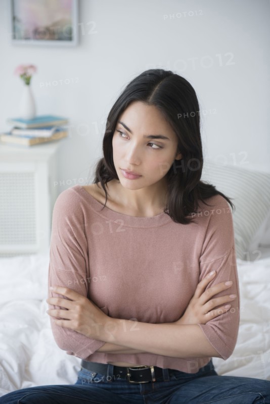 Frustrated Hispanic woman sitting on bed