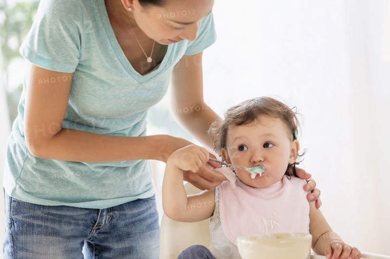 Mother feeding baby daughter in high chair