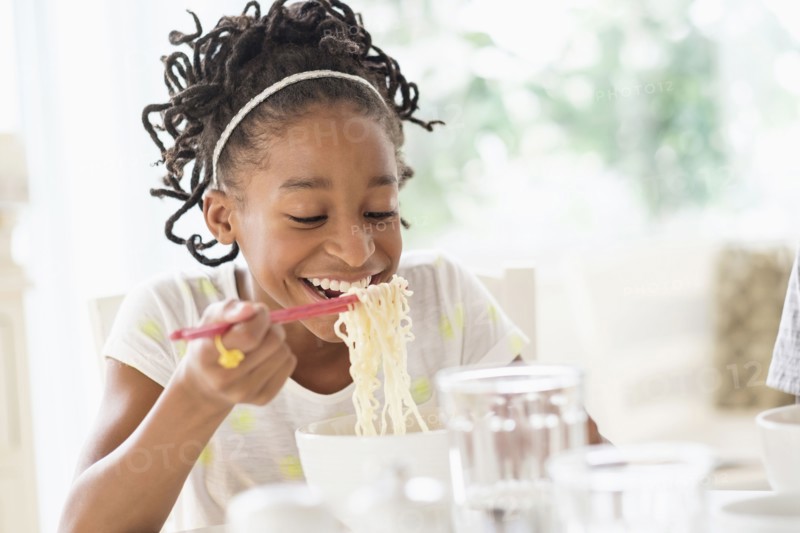 Black girl eating noodles at table