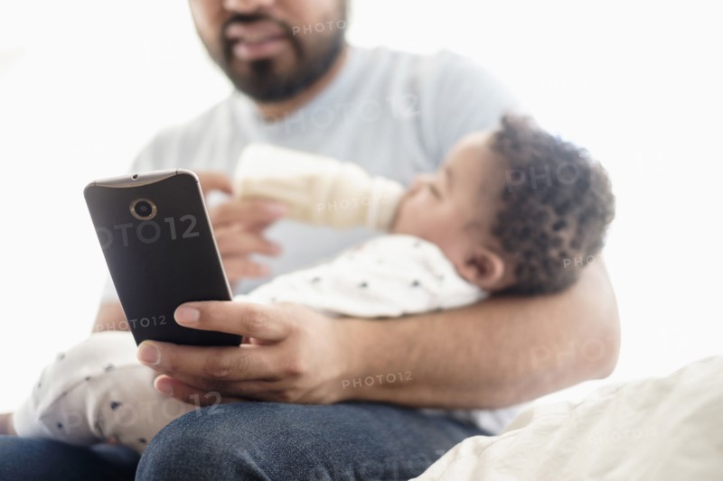 Father bottle feeding baby son and using cell phone
