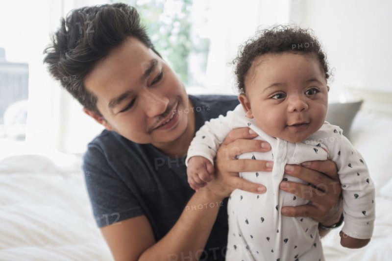 Father holding baby son on bed