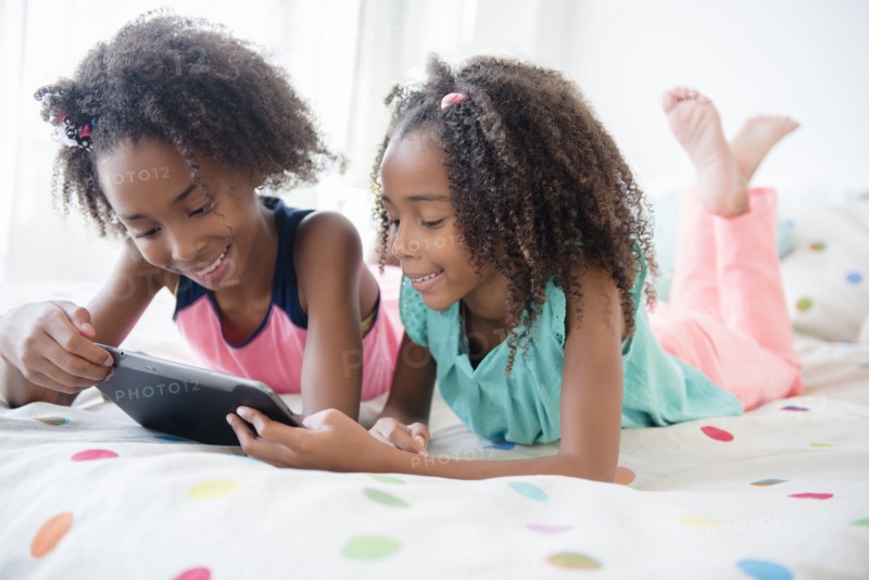 Mixed race sisters using digital tablet on bed