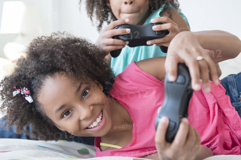Mixed race sisters playing video games on bed
