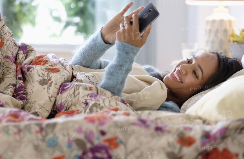 Mixed race woman using cell phone in bed