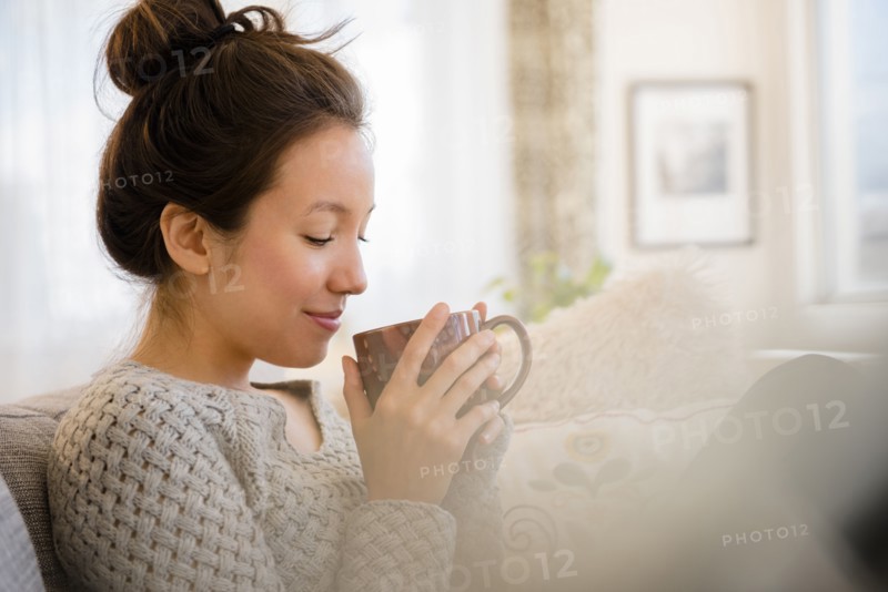 Mixed race woman drinking coffee on sofa