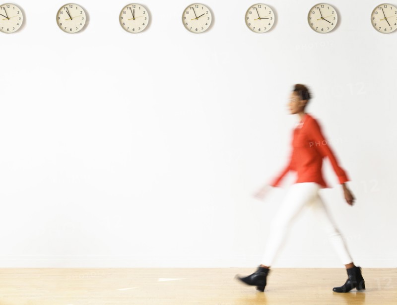 Mixed race businesswoman walking under clocks