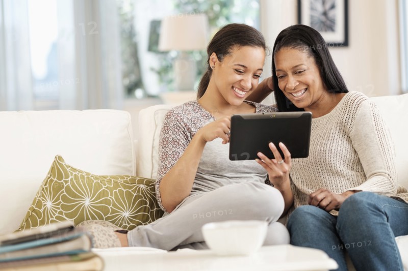 Mother and daughter using digital tablet on sofa