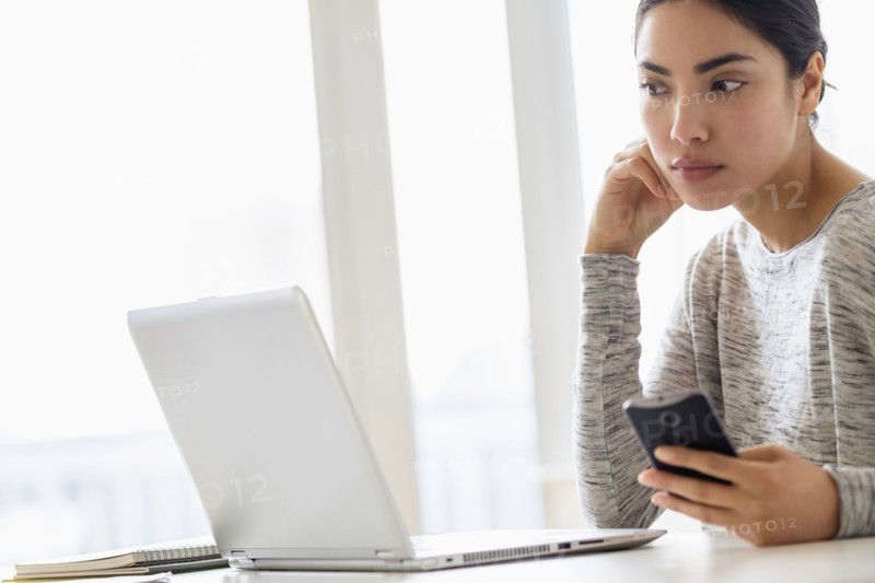 Hispanic woman using cell phone and laptop