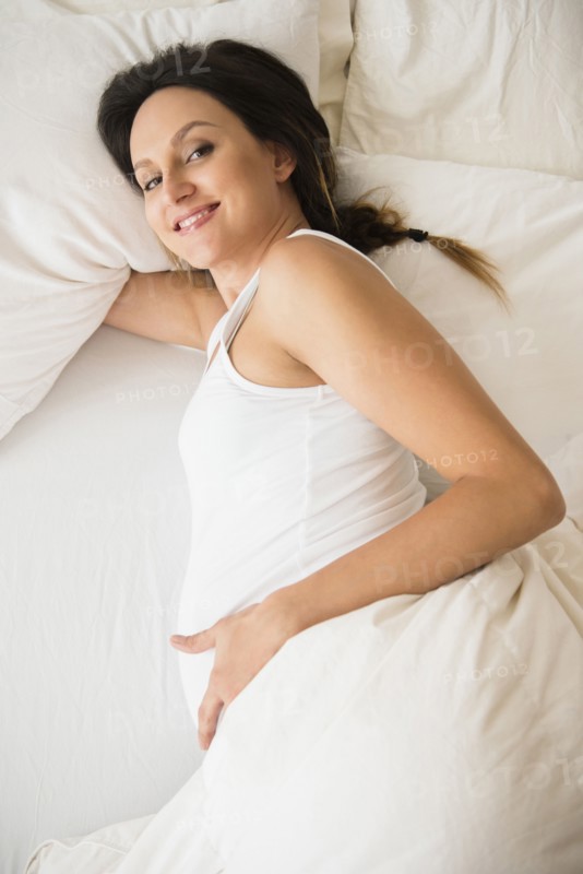 Pregnant Caucasian woman laying on bed