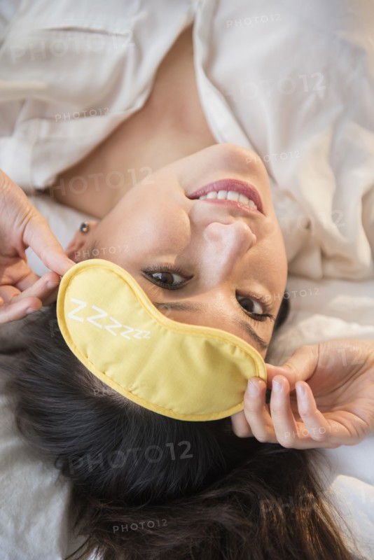 Smiling woman wearing eye mask on bed