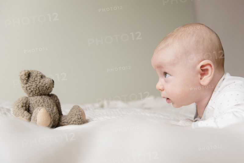 Caucasian baby staring at teddy bear on bed