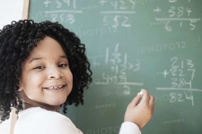 African American student writing on chalkboard in classroom
