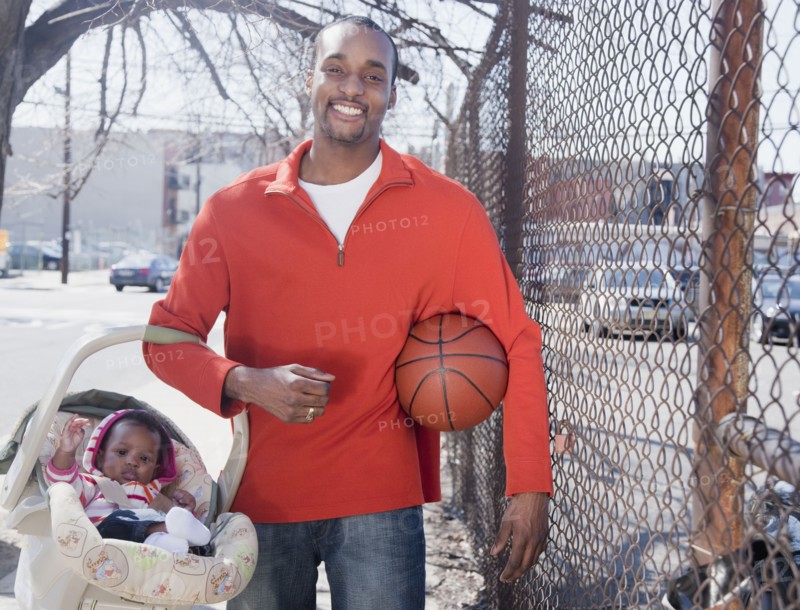 African man carrying baby in carrier and holding basketball
