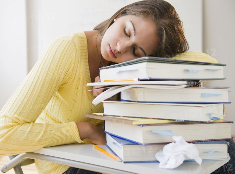 Tired Indian student laying on stack of textbooks