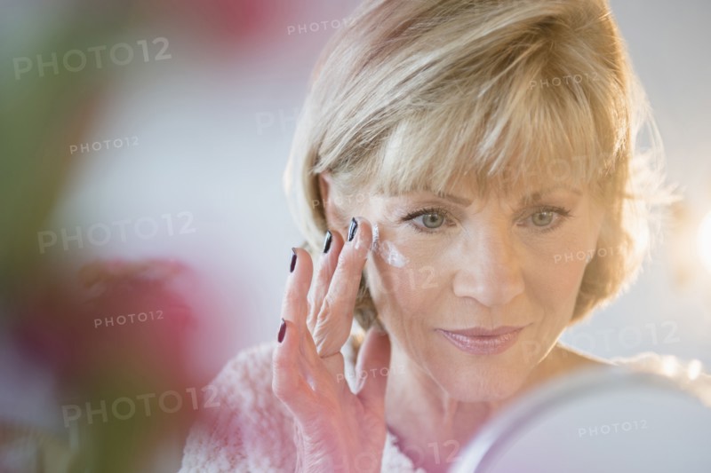 Older Caucasian woman applying moisturizer to face