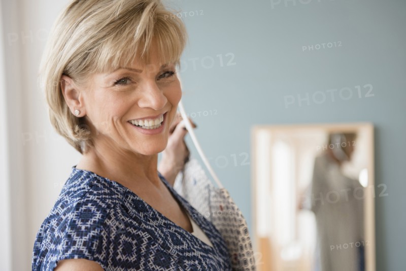 Smiling older Caucasian woman holding clothing near mirror