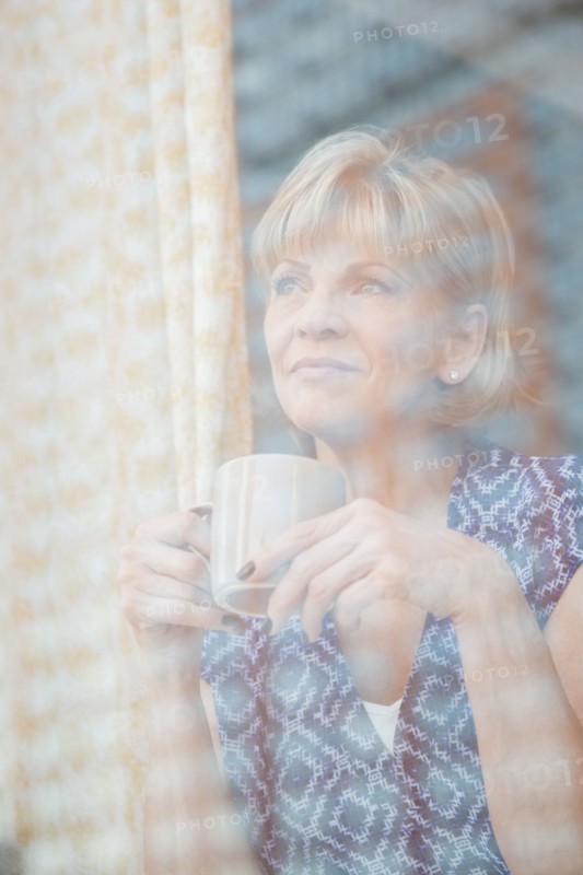 Older Caucasian woman drinking coffee at window