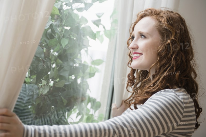 Caucasian woman opening curtains at window