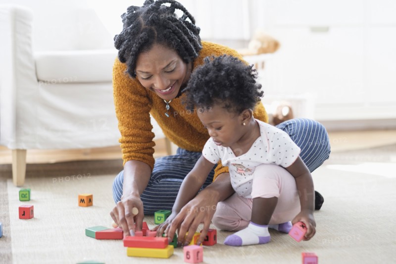 Black mother and baby daughter playing with blocks on carpet