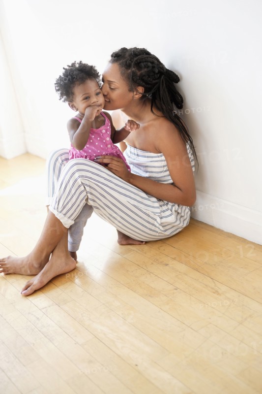 Black woman sitting on floor kissing cheek of baby daughter