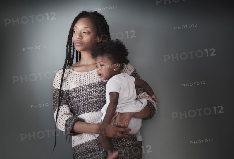Thoughtful Black woman standing holding baby daughter