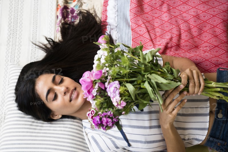 Indian woman laying on bed holding bouquet of flowers