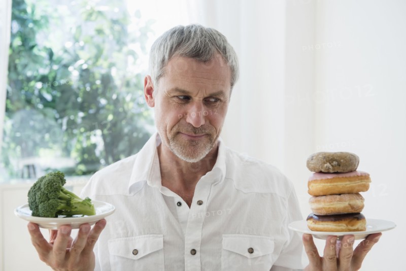 Older Caucasian man choosing between broccoli and donuts