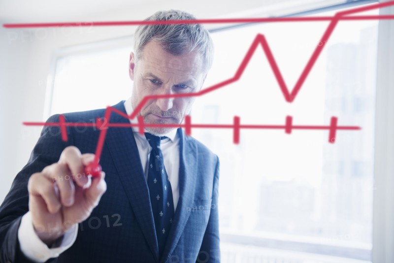 Older Caucasian businessman drawing chart on glass wall
