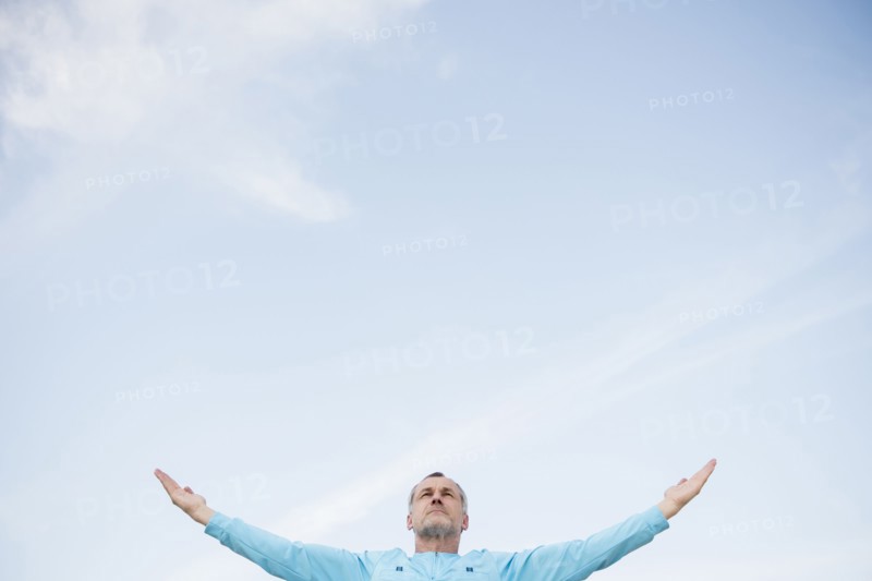 Older Caucasian man with arms outstretched against blue sky