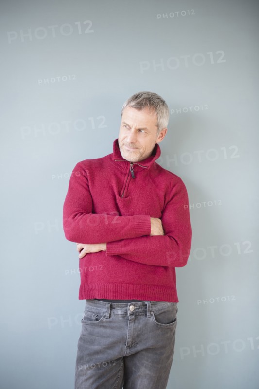 Older Caucasian man wearing sweater leaning on wall