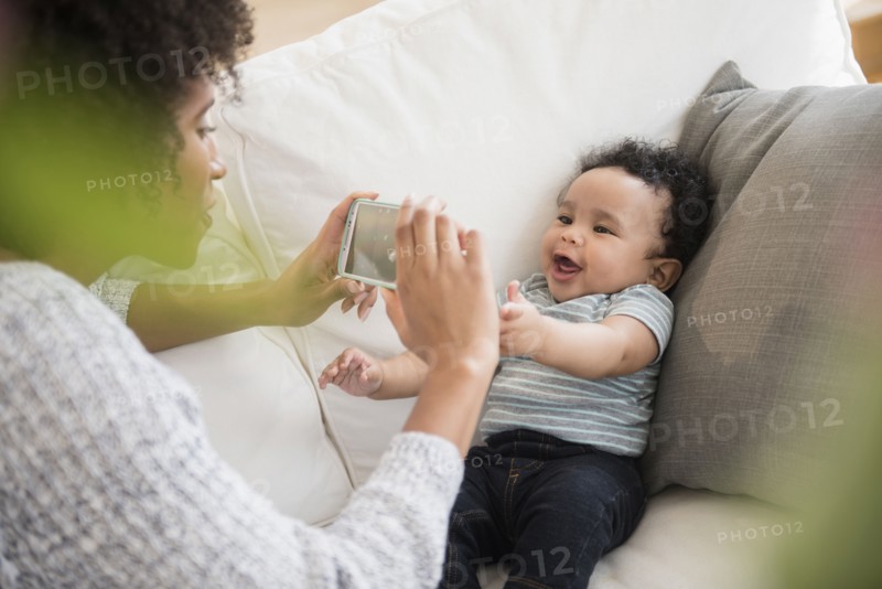 Mother photographing baby son with cell phone on sofa