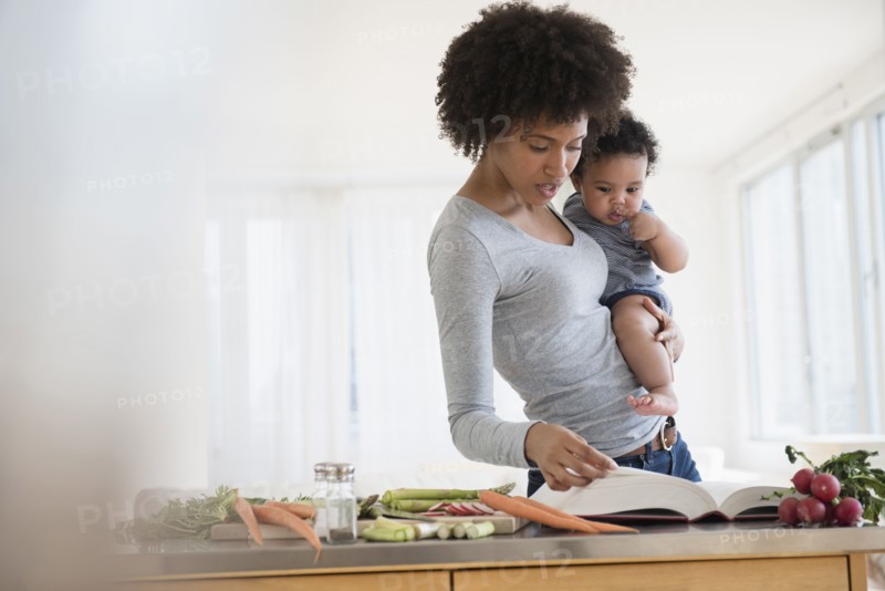 Mother reading cookbook while holding baby son