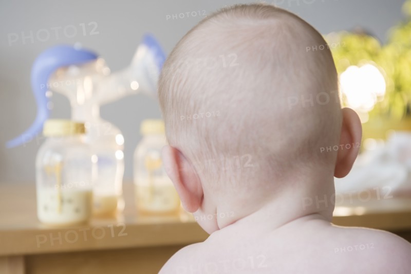 Caucasian baby boy looking at bottles of breast milk