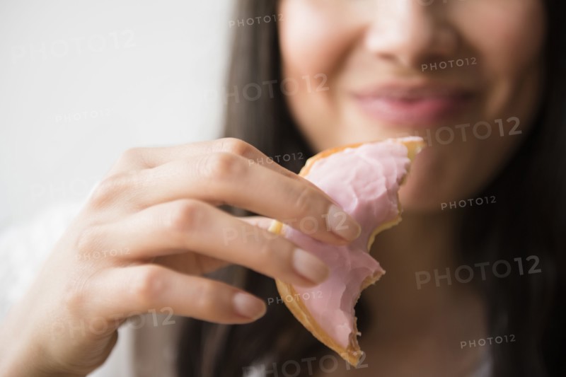 Hispanic woman eating donut with pink icing