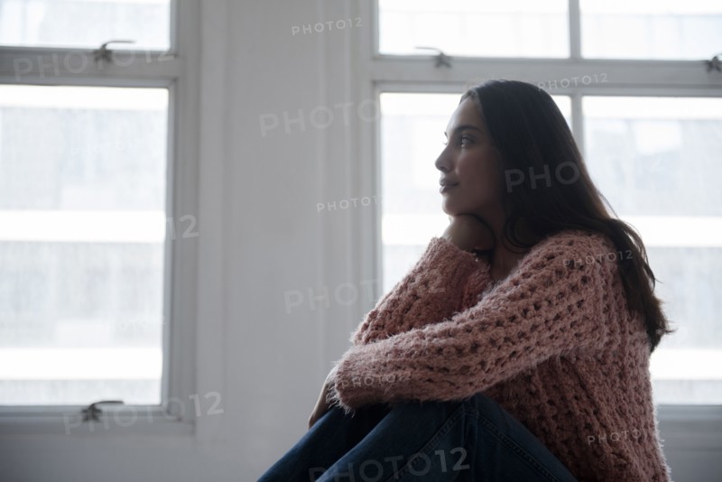 Hispanic woman wearing pink sweater and jeans near window