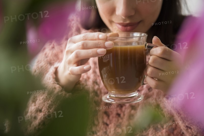 Hispanic woman drinking coffee behind flowers