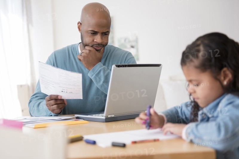 Daughter coloring with crayons while father uses laptop