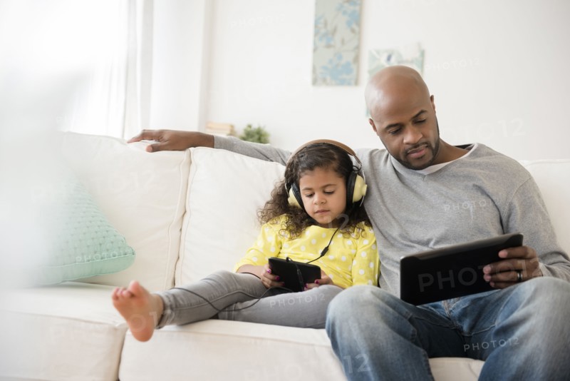 Father and daughter using digital tablets on sofa
