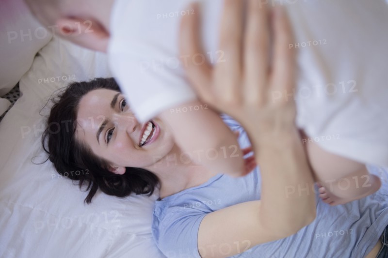 Caucasian mother laying on bed lifting baby son