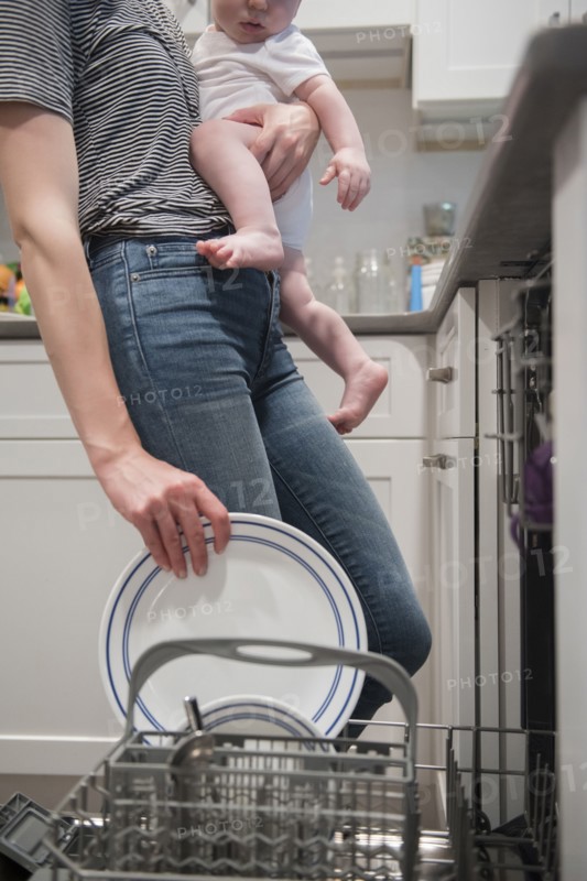 Caucasian mother holding baby son holding plate in dishwasher