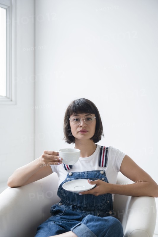 Portrait of Hispanic woman drinking coffee in armchair