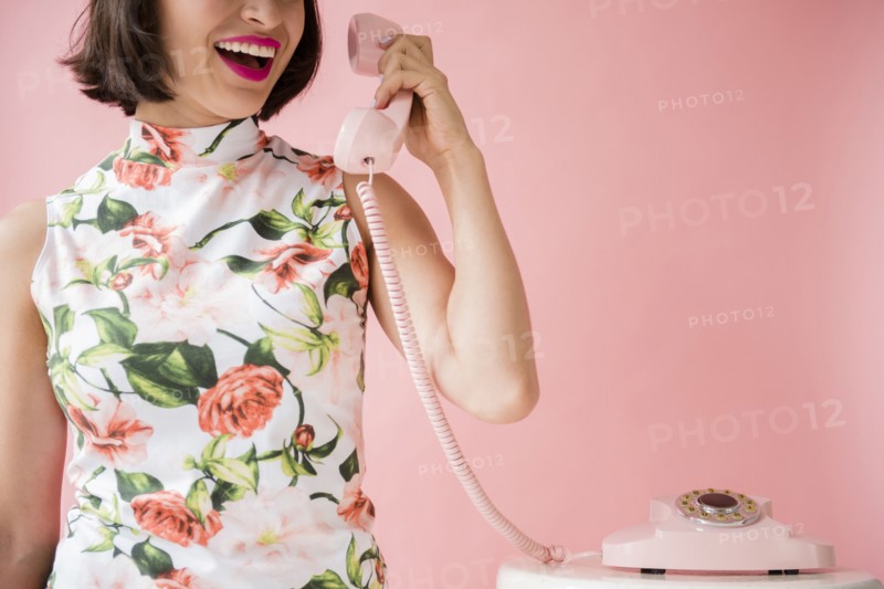 Hispanic woman wearing floral dress holding pink telephone