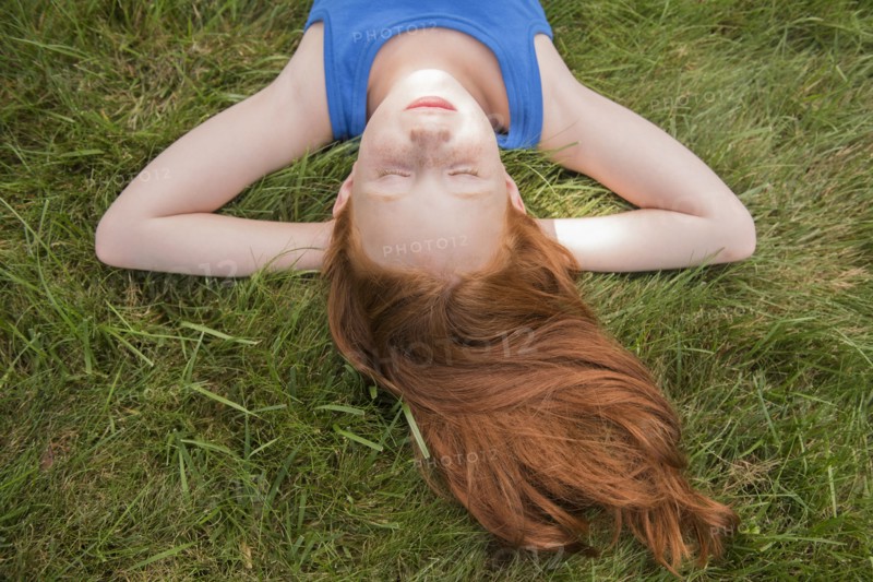 Caucasian girl laying in grass with hands behind head