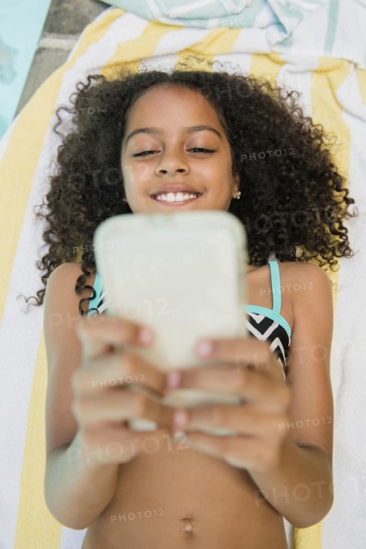 Smiling Hispanic girl texting on cell phone at swimming pool