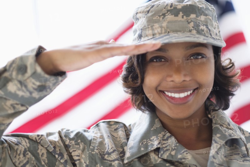 Portrait of smiling Mixed Race soldier saluting near American flag