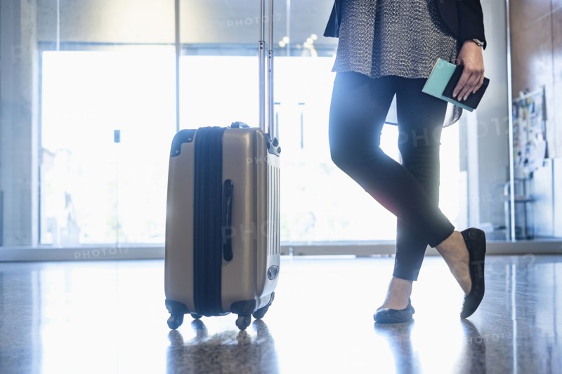 Hispanic woman holding passport standing with suitcase in airport