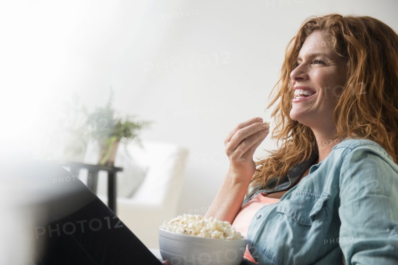 Laughing Caucasian woman eating bowl of popcorn
