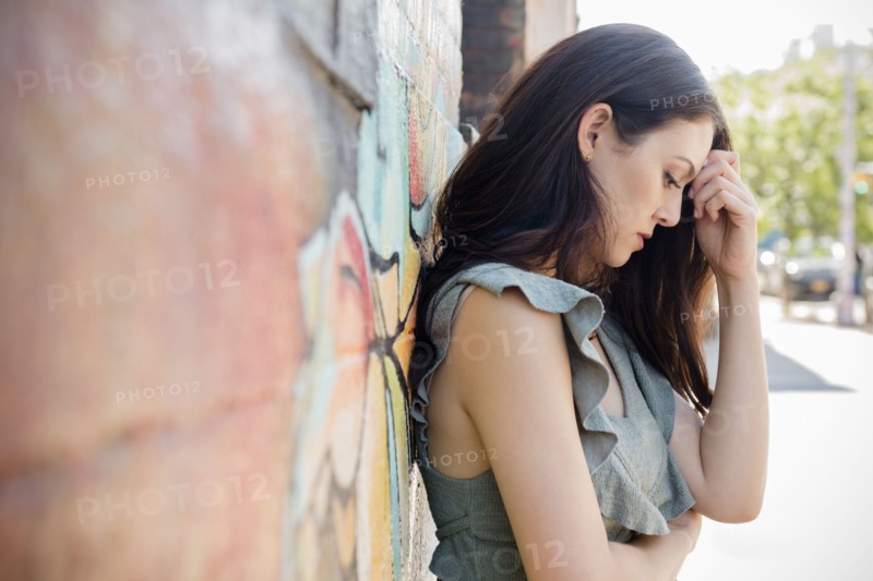 Worried Thai woman leaning on wall in city