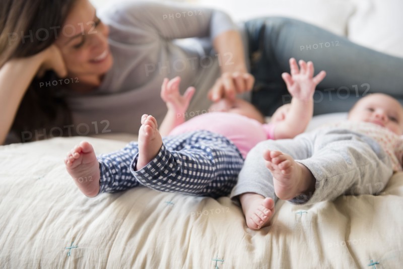 Caucasian mother playing with twin baby daughters on bed