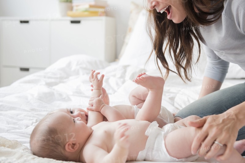Caucasian mother playing with twin baby daughters on bed
